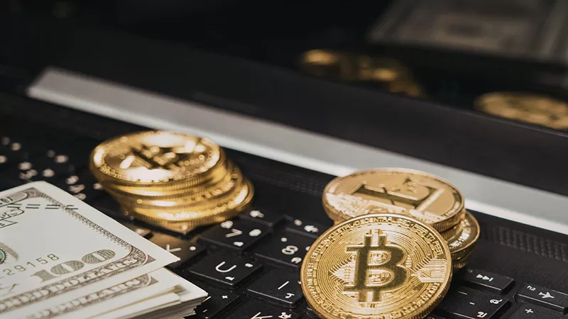 Golden bitcoin coins and paper currency displayed on a laptop keyboard, representing digital cryptocurrency and financial technology investment concepts