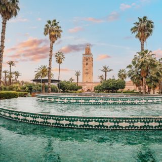 The majestic Koutoubia Mosque rises above a serene fountain in Marrakech, Morocco, bathed in the warm glow of the setting sun