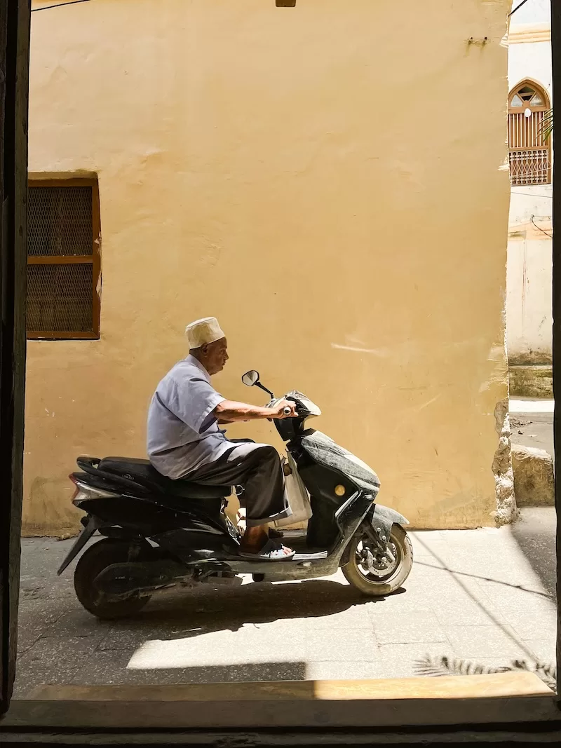 A vibrant street scene in Stone Town where local vendors and residents interact amidst historic architecture, reflecting the city's living Swahili culture.