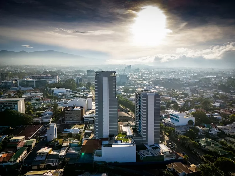 An aerial view of modern high-rise buildings in San Jose, Costa Rica, under a bright sun, representing the country's urban development and modernization.