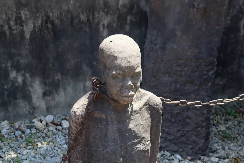 A somber stone sculpture of enslaved people in chains at the East Africa Slave Trade Exhibition in Stone Town, memorializing Zanzibar's poignant history.