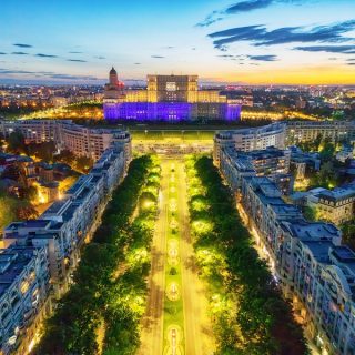 A red cable car descends from a lush green mountain, offering a breathtaking aerial view of the historic red-tiled roofs of Brasov, Romania, under a cloudy sky.