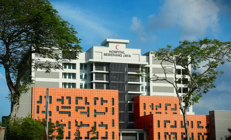 The modern, multi-story Hospital Seberang Jaya building in Malaysia features a clean white facade with vibrant orange accents under a bright blue sky.