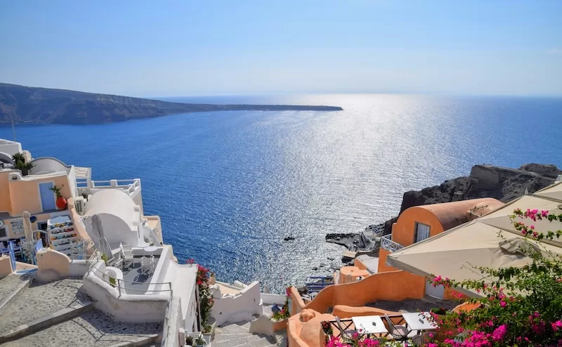A scenic view of white buildings with blue and orange accents perched on the cliffs of Santorini, Greece, overlooking the vast, deep blue Mediterranean Sea.