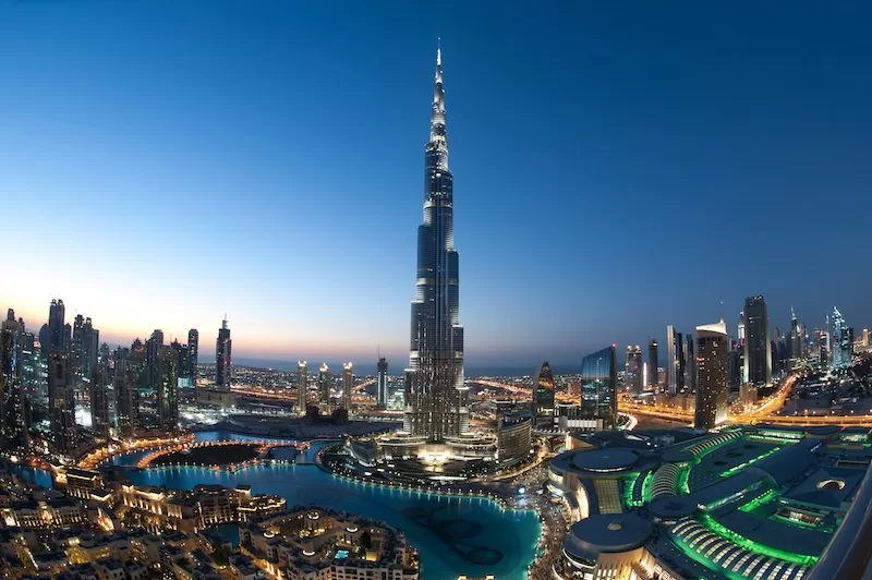 Burj Khalifa towering above the illuminated Dubai skyline at dusk with surrounding skyscrapers and fountains.