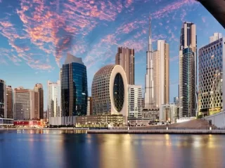 Iranian flag waving on a pole with Tehran cityscape and mountains in background, representing Iran-US geopolitical tensions and Middle East conflict