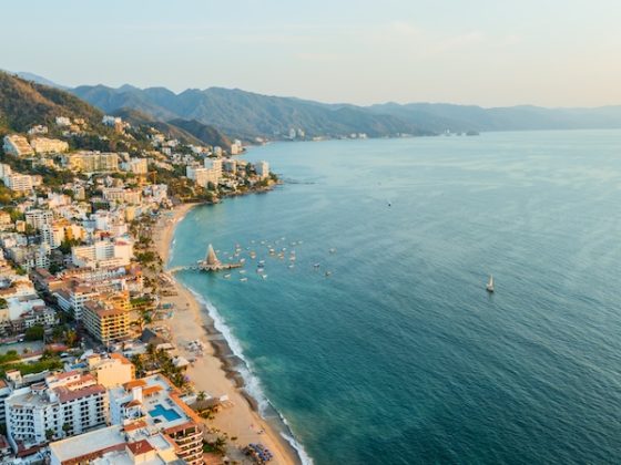 Aerial view of Puerto Vallarta coastal town with turquoise ocean water, sandy beaches, white buildings, green mountains, and boats anchored in the bay