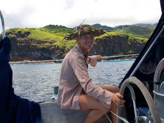 Woman steering a sailboat near a tropical island while living a sailing lifestyle at sea