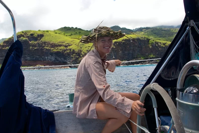 Woman steering a sailboat near a tropical island while living a sailing lifestyle at sea