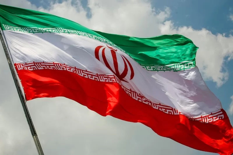 Iranian national flag waving against the sky with its green, white, and red horizontal stripes.