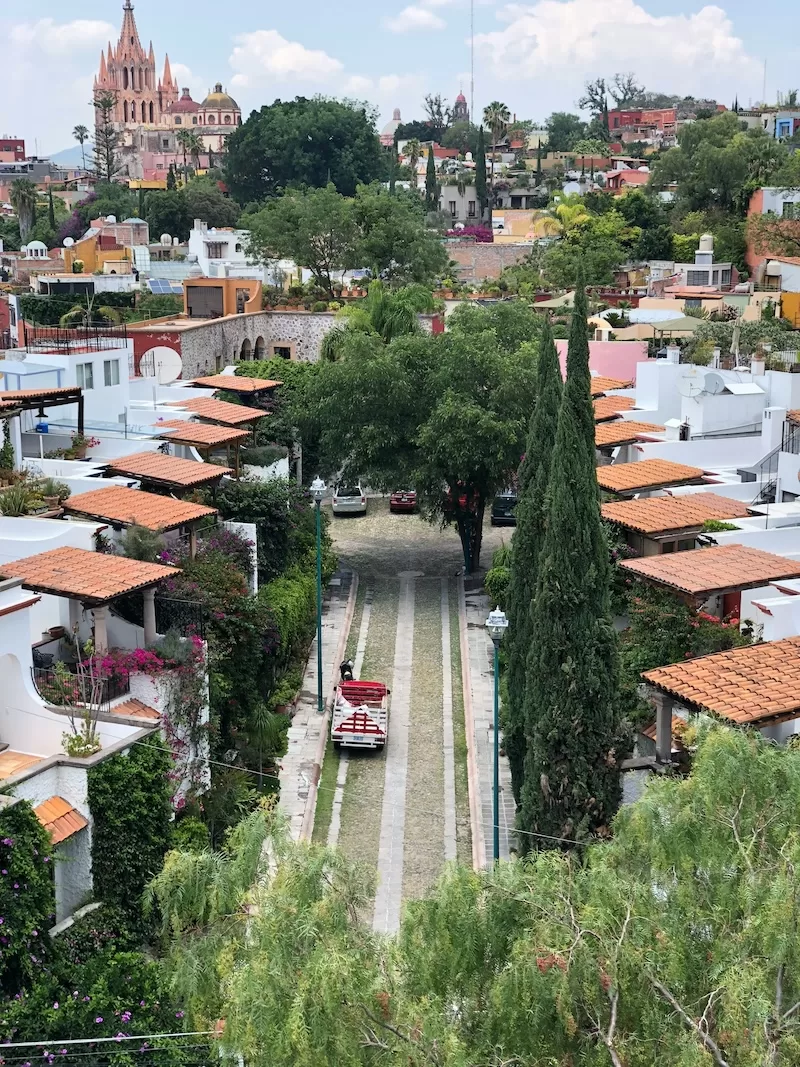 Colorful colonial architecture in a Mexican city with pink cathedral, white buildings, red tile roofs, green vegetation, and a red vintage car on a street