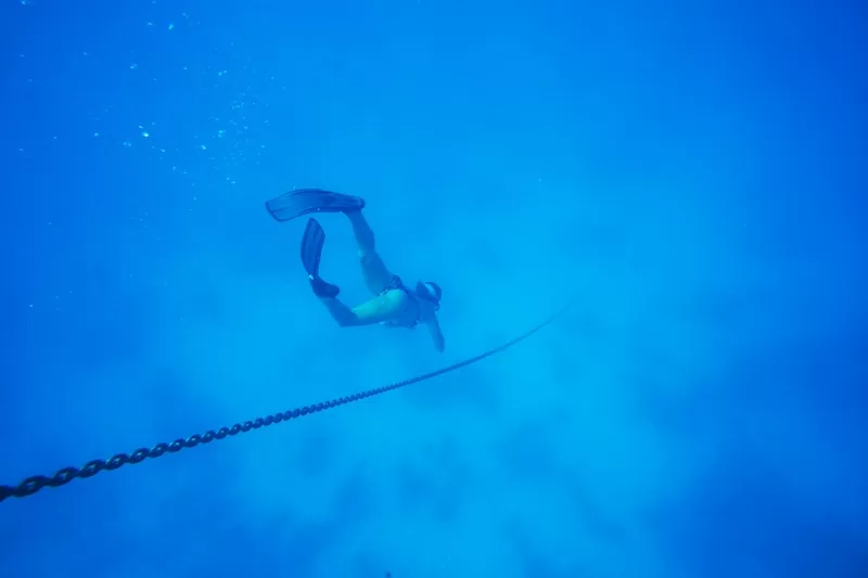 Freediver descending into deep blue ocean water during a sailing expedition