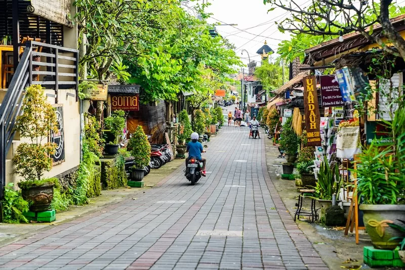 Local street in Bali with shops, greenery, and motorbike traffic