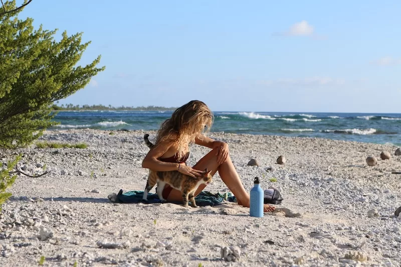 Woman relaxing on a remote tropical beach with a cat during island travel