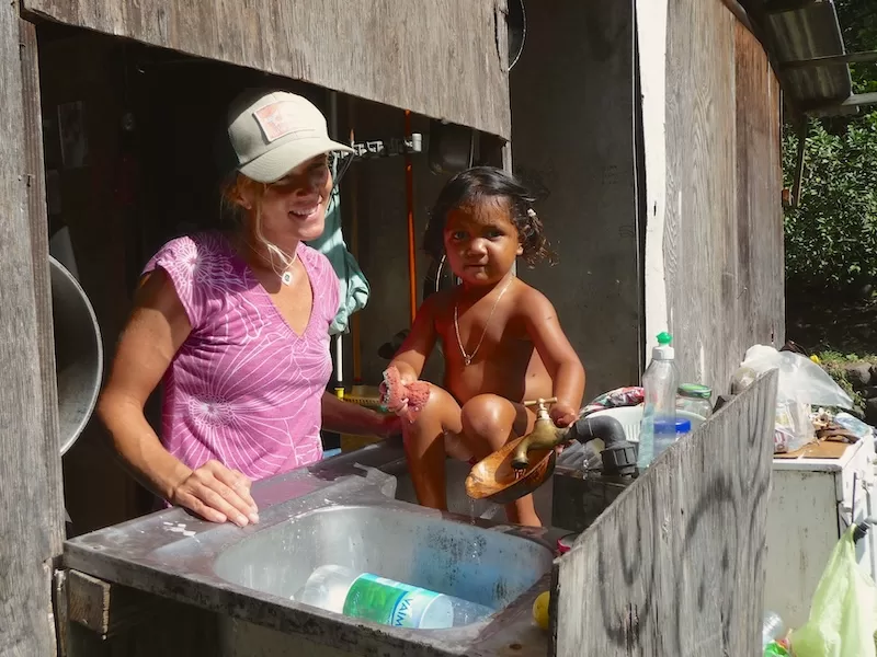 Woman and child washing dishes in a rustic outdoor kitchen during island life