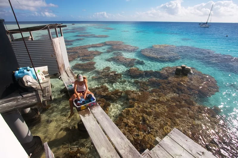 Woman washing clothes on wooden dock above clear turquoise ocean water
