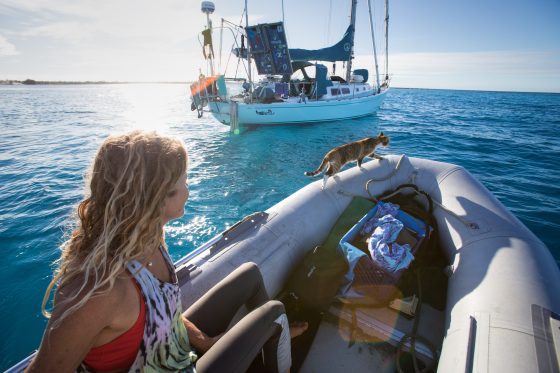 Woman steering a sailboat near a tropical island while living a sailing lifestyle at sea