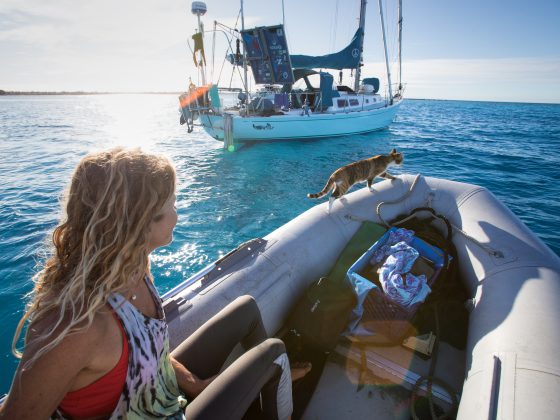 Woman steering a sailboat near a tropical island while living a sailing lifestyle at sea
