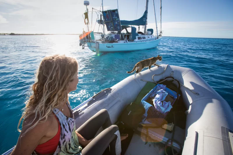 Woman steering a sailboat near a tropical island while living a sailing lifestyle at sea