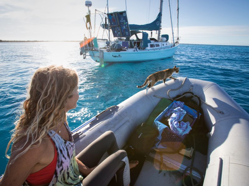 Woman steering a sailboat near a tropical island while living a sailing lifestyle at sea
