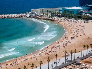 Crowded Barceloneta Beach with clear blue-green sea. View from above.