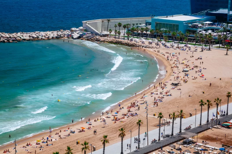 Crowded Barceloneta Beach with clear blue-green sea. View from above.