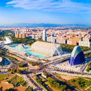 Aerial view of Valencia’s City of Arts and Sciences with modern architecture, blue pools, and the wider city skyline under a bright sky