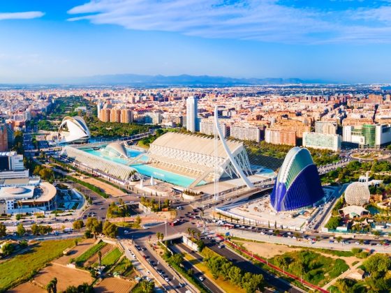Aerial view of Valencia’s City of Arts and Sciences with modern architecture, blue pools, and the wider city skyline under a bright sky