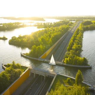 Aerial view of a roadway and bridge cutting through bright waterways and tree-lined islands at sunset in the Netherlands