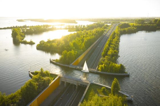 Aerial view of a roadway and bridge cutting through bright waterways and tree-lined islands at sunset in the Netherlands