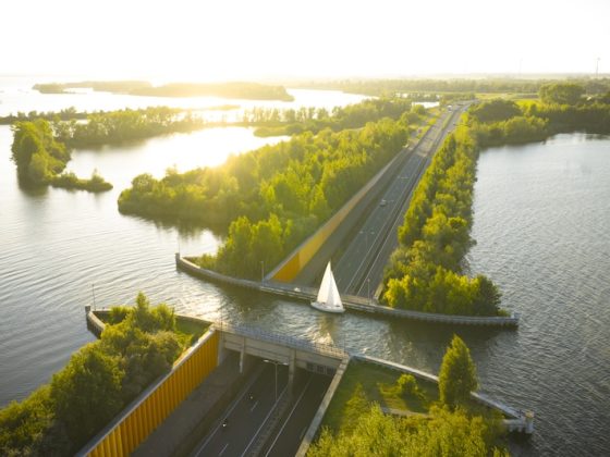 Aerial view of a roadway and bridge cutting through bright waterways and tree-lined islands at sunset in the Netherlands