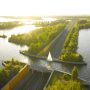 Aerial view of a roadway and bridge cutting through bright waterways and tree-lined islands at sunset in the Netherlands