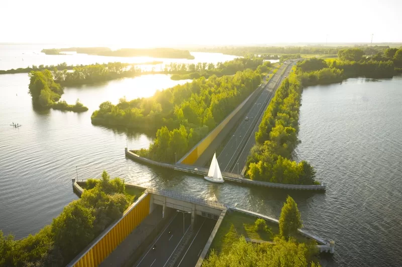 Aerial view of a roadway and bridge cutting through bright waterways and tree-lined islands at sunset in the Netherlands