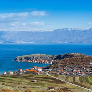 Rural village and farmland beside a bright blue lake in North Macedonia with mountains in the distance.
