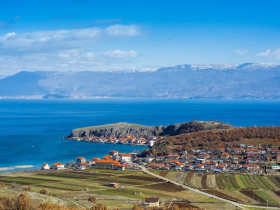 Rural village and farmland beside a bright blue lake in North Macedonia with mountains in the distance.