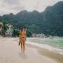 Woman walking barefoot along a beach in the Philippines with boats, waterfront buildings, and lush limestone hills in the background