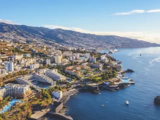 Aerial view of a coastal Portuguese city with hotels, residential buildings, mountains, and the Atlantic shoreline stretching into the distance