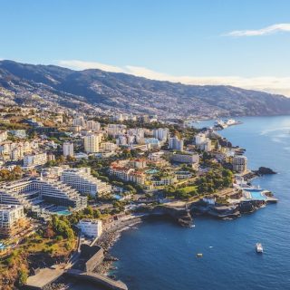 Aerial view of a coastal Portuguese city with hotels, residential buildings, mountains, and the Atlantic shoreline stretching into the distance