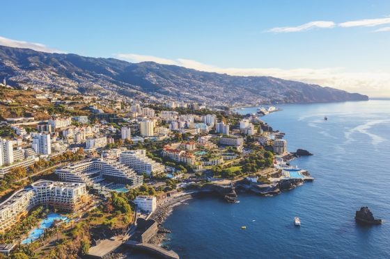 Aerial view of a coastal Portuguese city with hotels, residential buildings, mountains, and the Atlantic shoreline stretching into the distance