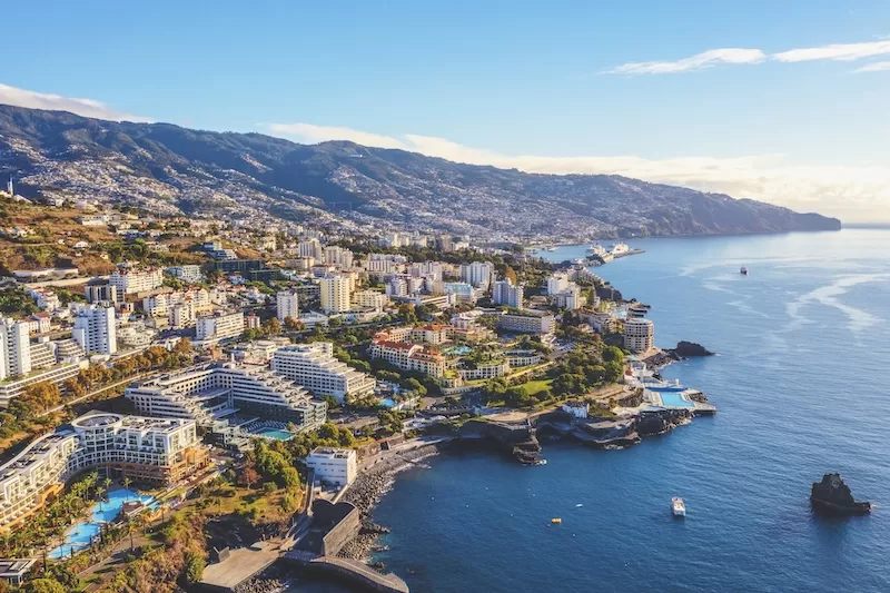 Aerial view of a coastal Portuguese city with hotels, residential buildings, mountains, and the Atlantic shoreline stretching into the distance