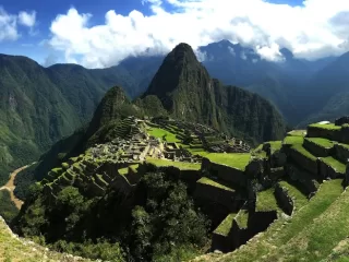 Wide view of Machu Picchu with green terraced ruins set high among dramatic Andes mountains under a bright sky
