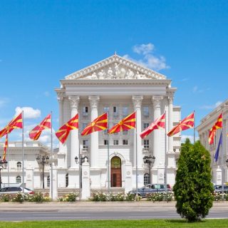 Government building in Skopje with rows of North Macedonian flags flying in front.