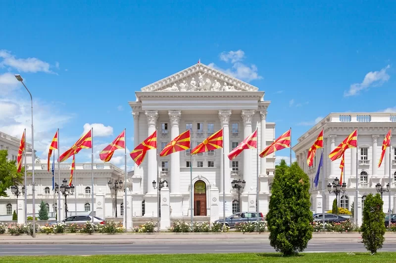 Government building in Skopje with rows of North Macedonian flags flying in front.