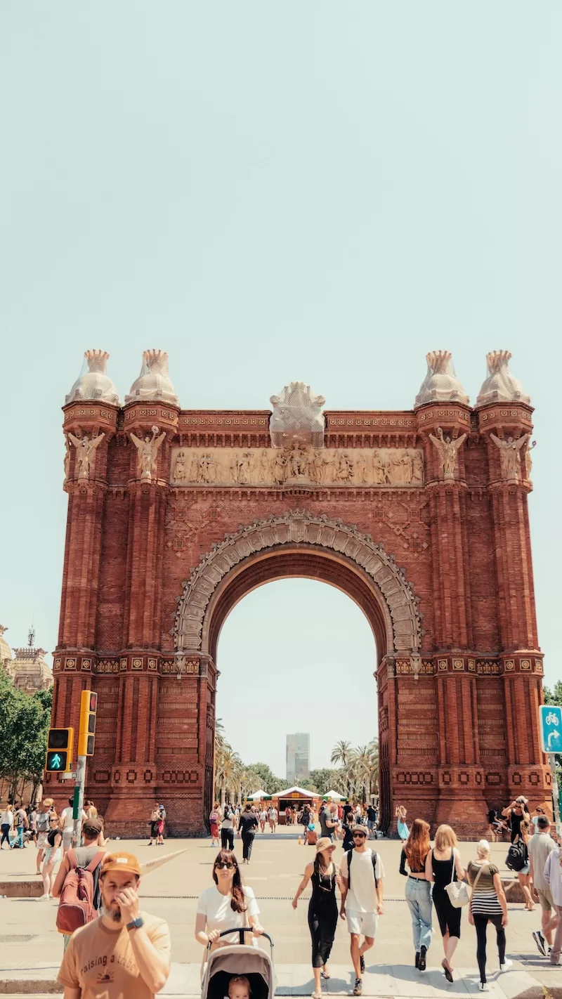 Pedestrians walking beneath the Arc de Triomf in Barcelona on a bright day.