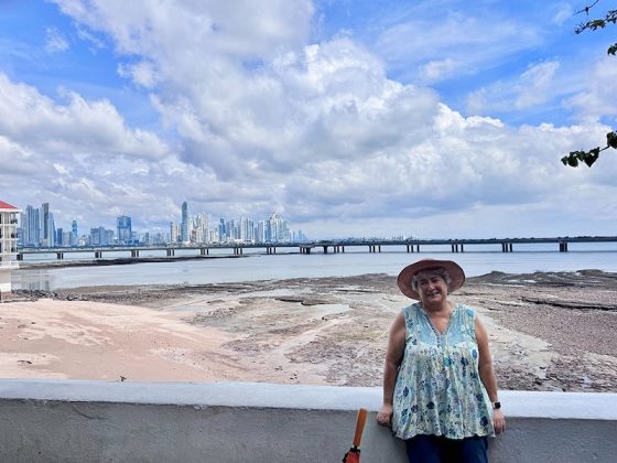 Woman in a sunhat standing by the waterfront with the Panama City skyline in the distance.