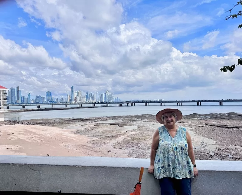 Woman in a sunhat standing by the waterfront with the Panama City skyline in the distance.