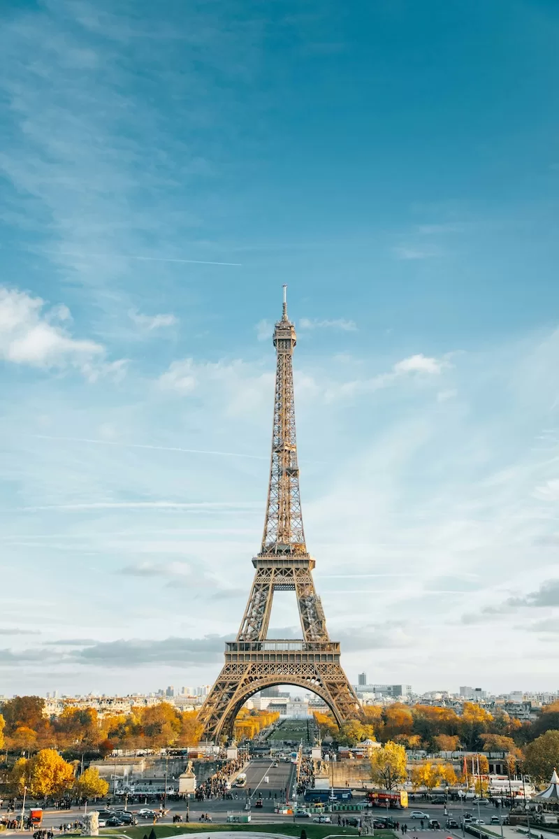Eiffel Tower rising above Paris under a clear blue sky with autumn trees and city streets visible below