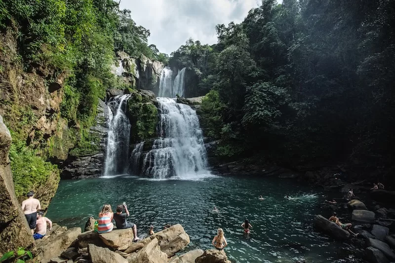 Large waterfall cascading into a jungle pool in Costa Rica with visitors swimming and relaxing on rocks below