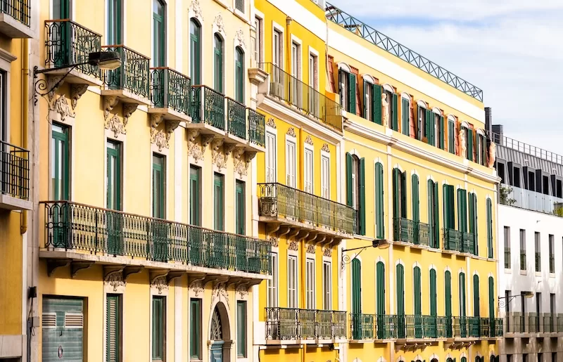 Elegant yellow historic building in Portugal with green shutters, wrought-iron balconies, and traditional architectural detailing