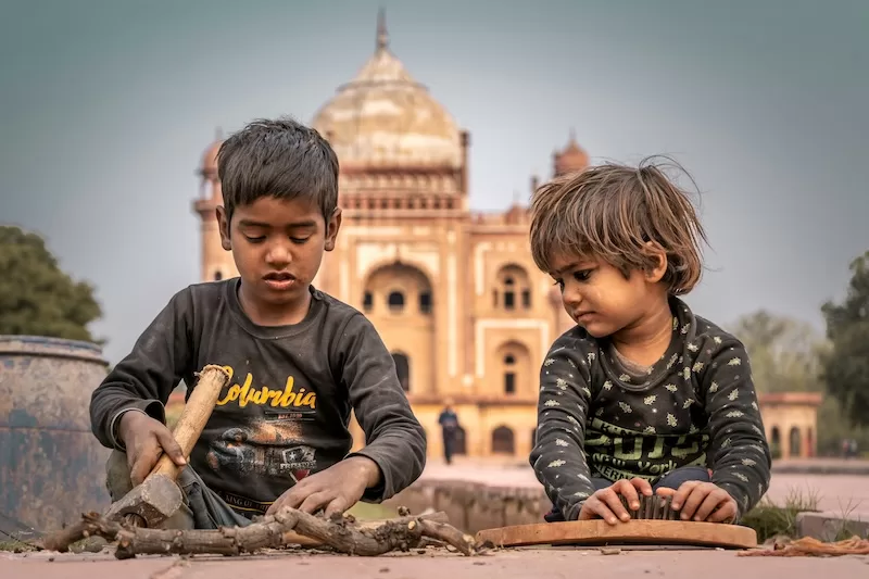 Two children working with sticks and tools in front of a large historic domed monument in India